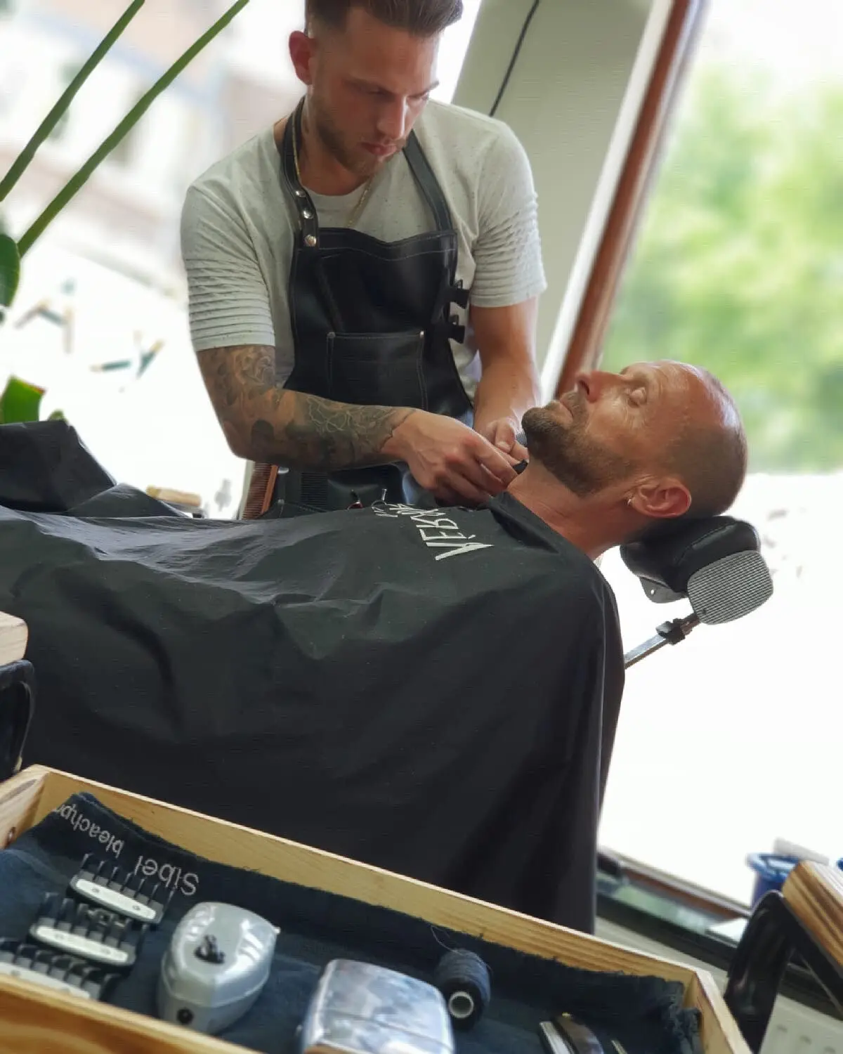 Barbier trimt de baard van een klant bij het raam