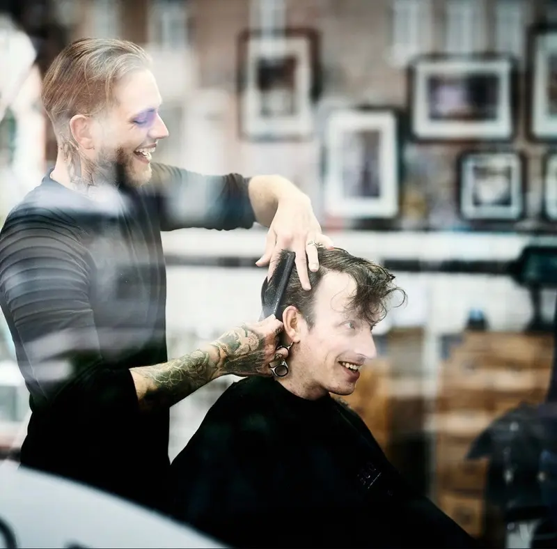 Klant lacht in de stoel terwijl de barbier knipt